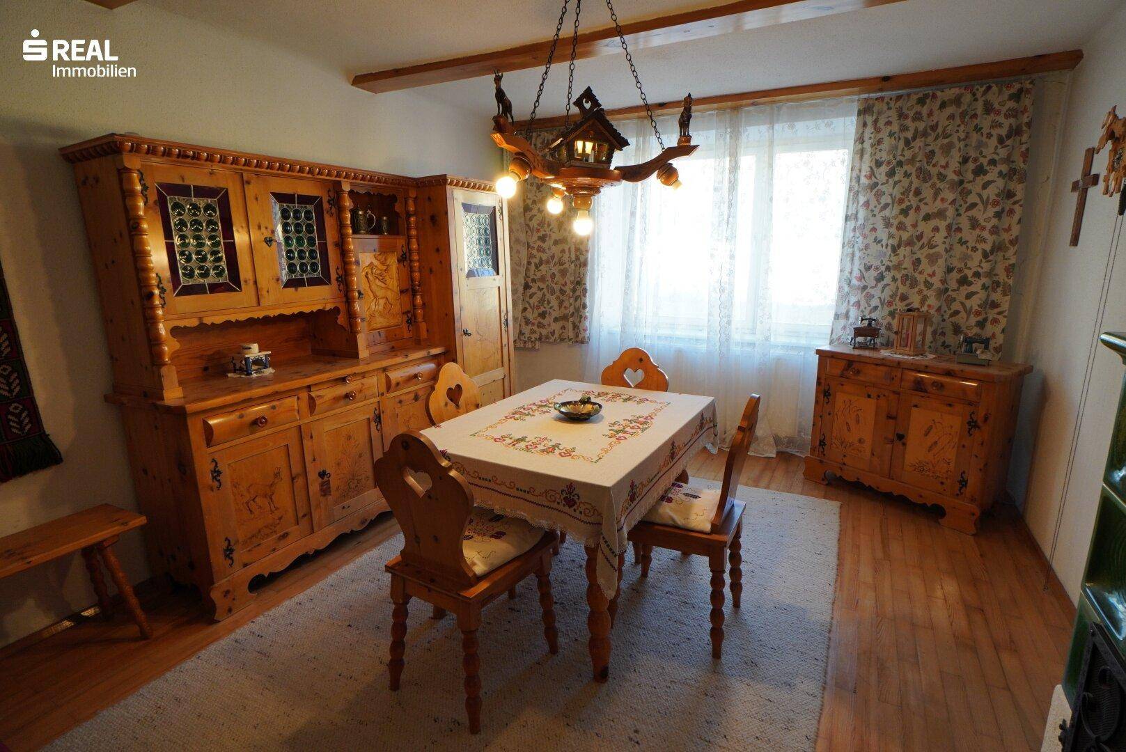 Esszimmer mit rustikalen Holzmöbeln, Holzboden und einem großen Fenster mit Vorhängen.