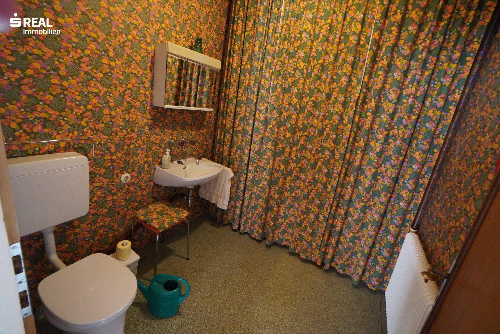 Kleines WC mit floraler Tapete, Waschbecken und Toilette.