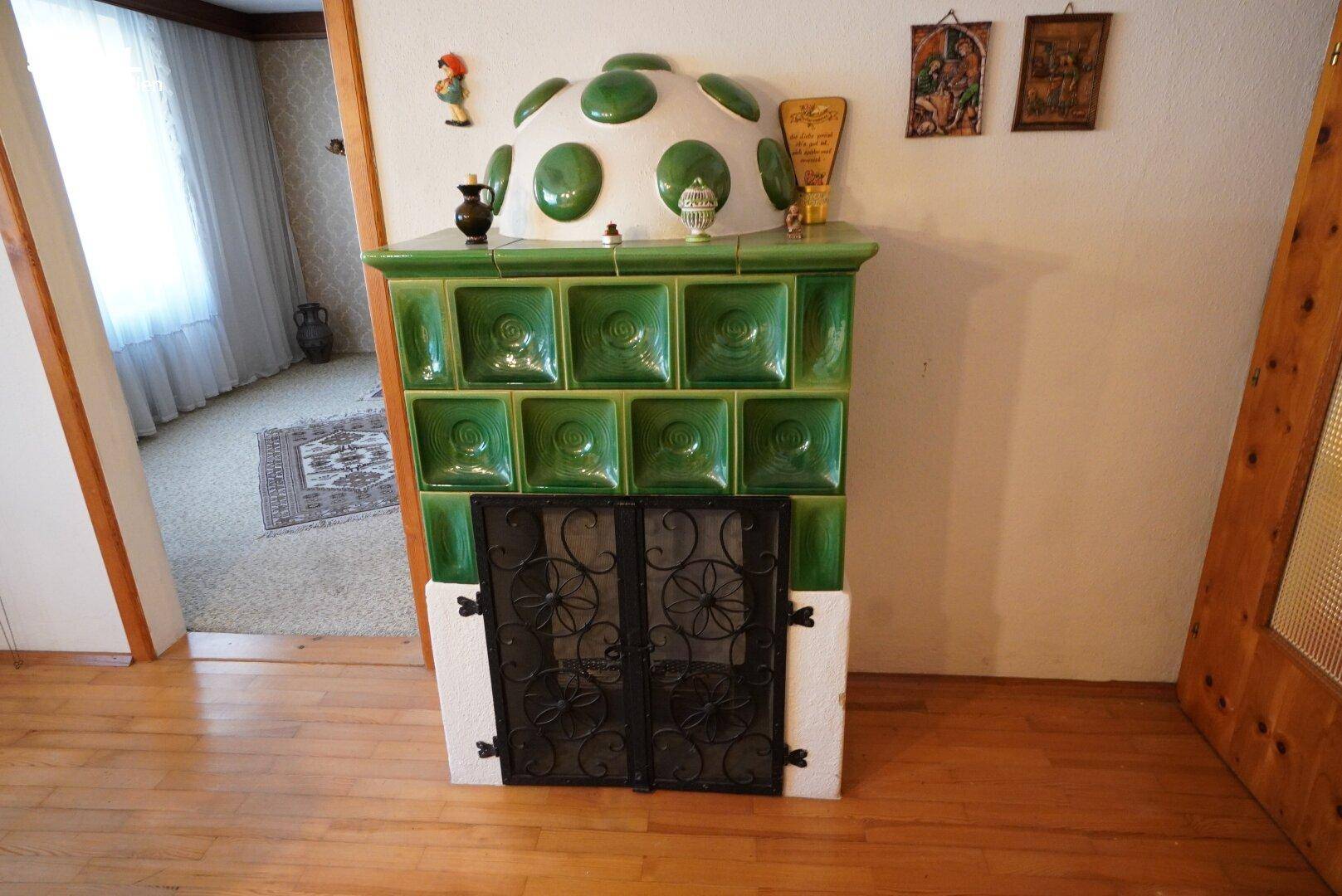 Grüner Kachelofen als traditionelles Heizelement im Wohnbereich mit Holzboden.