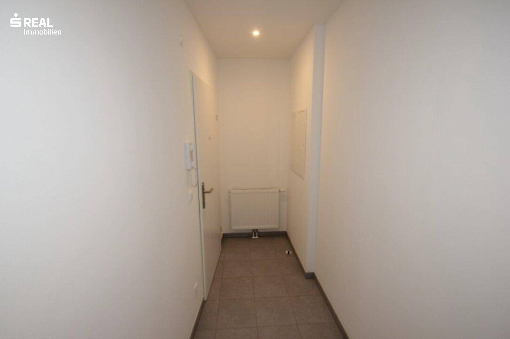 Schmaler, heller Flur mit Fliesenboden und Gegensprechanlage.