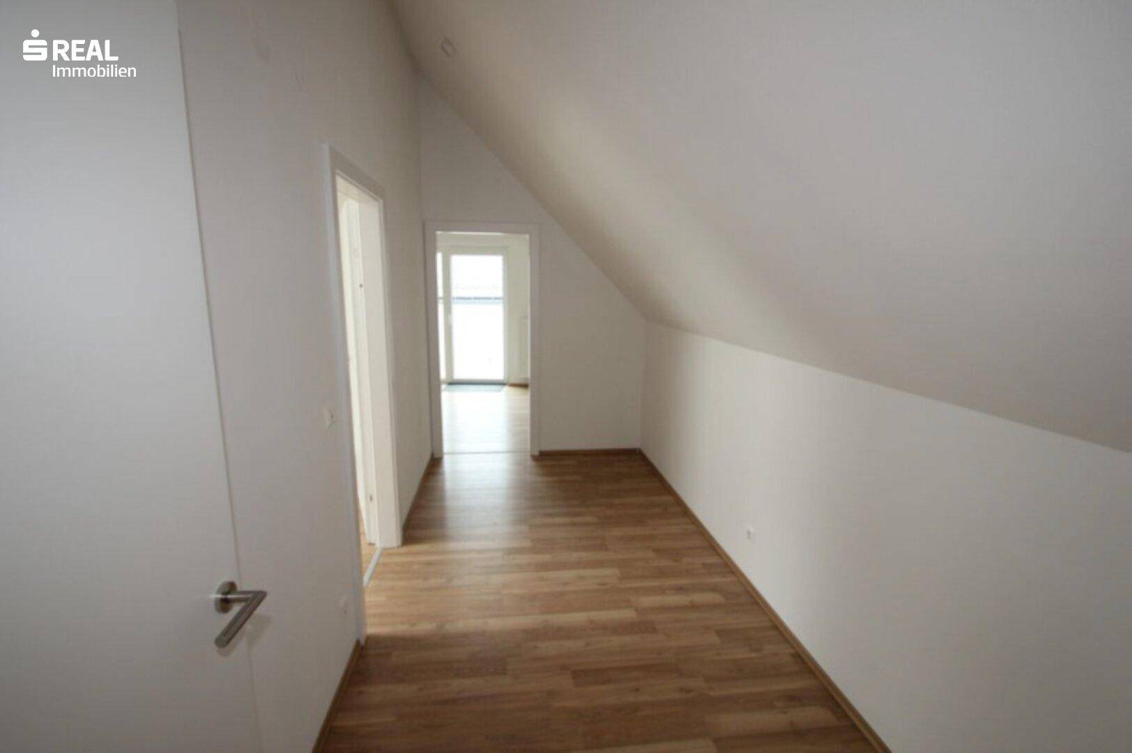 Heller Flur im Dachgeschoss mit Holzboden, der zu weiteren Räumen führt.