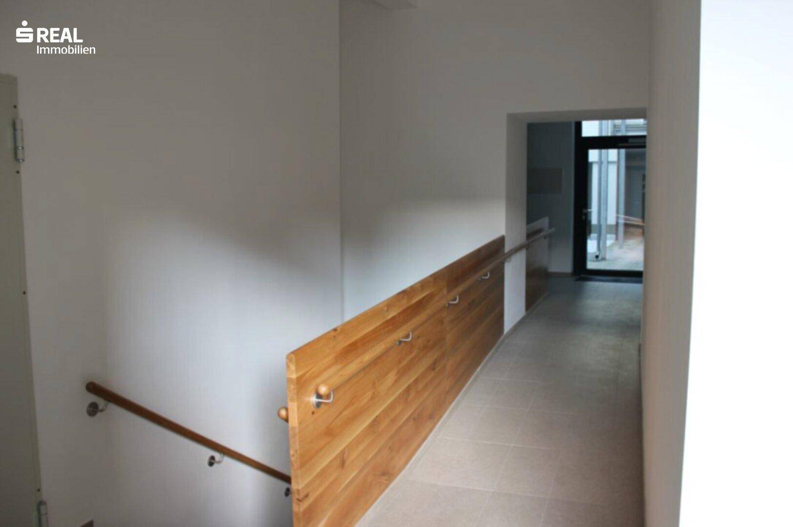 Heller Eingangsbereich mit Rampe und Treppe, ausgestattet mit Holzgeländer.
