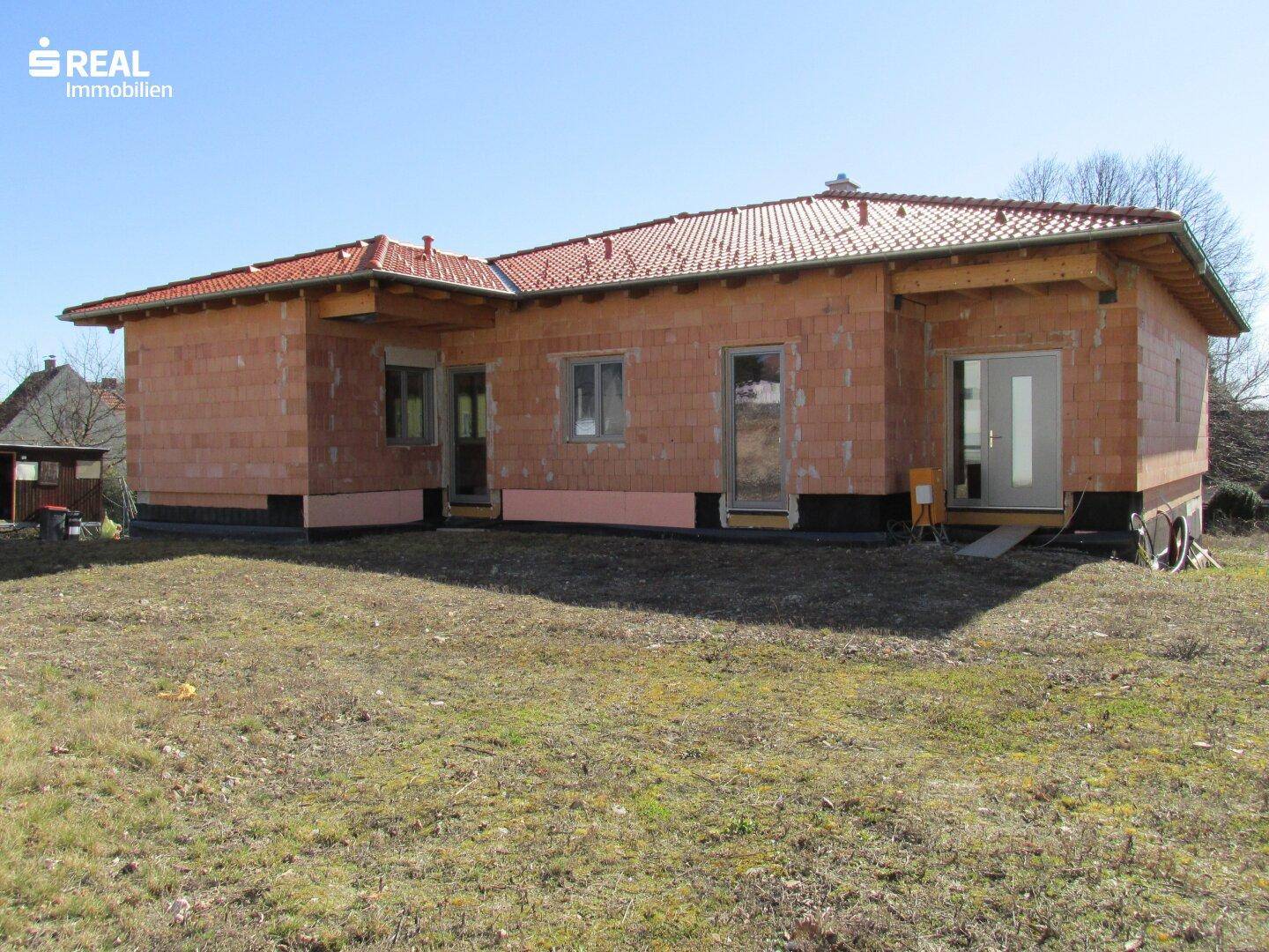 Neubau im Rohbau mit sichtbaren Ziegelwänden und Dachkonstruktion, umgeben von einer Wiese.