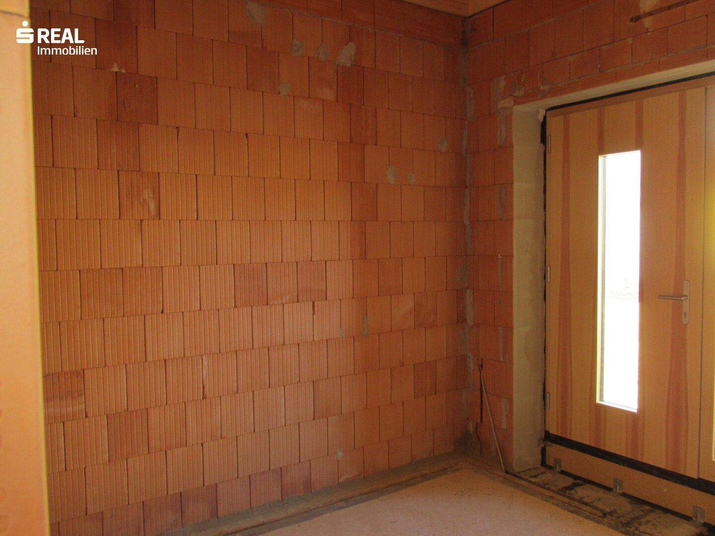 Innenraum im Rohbau mit Ziegelwänden und einer provisorischen Eingangstür, bereit für den Ausbau.