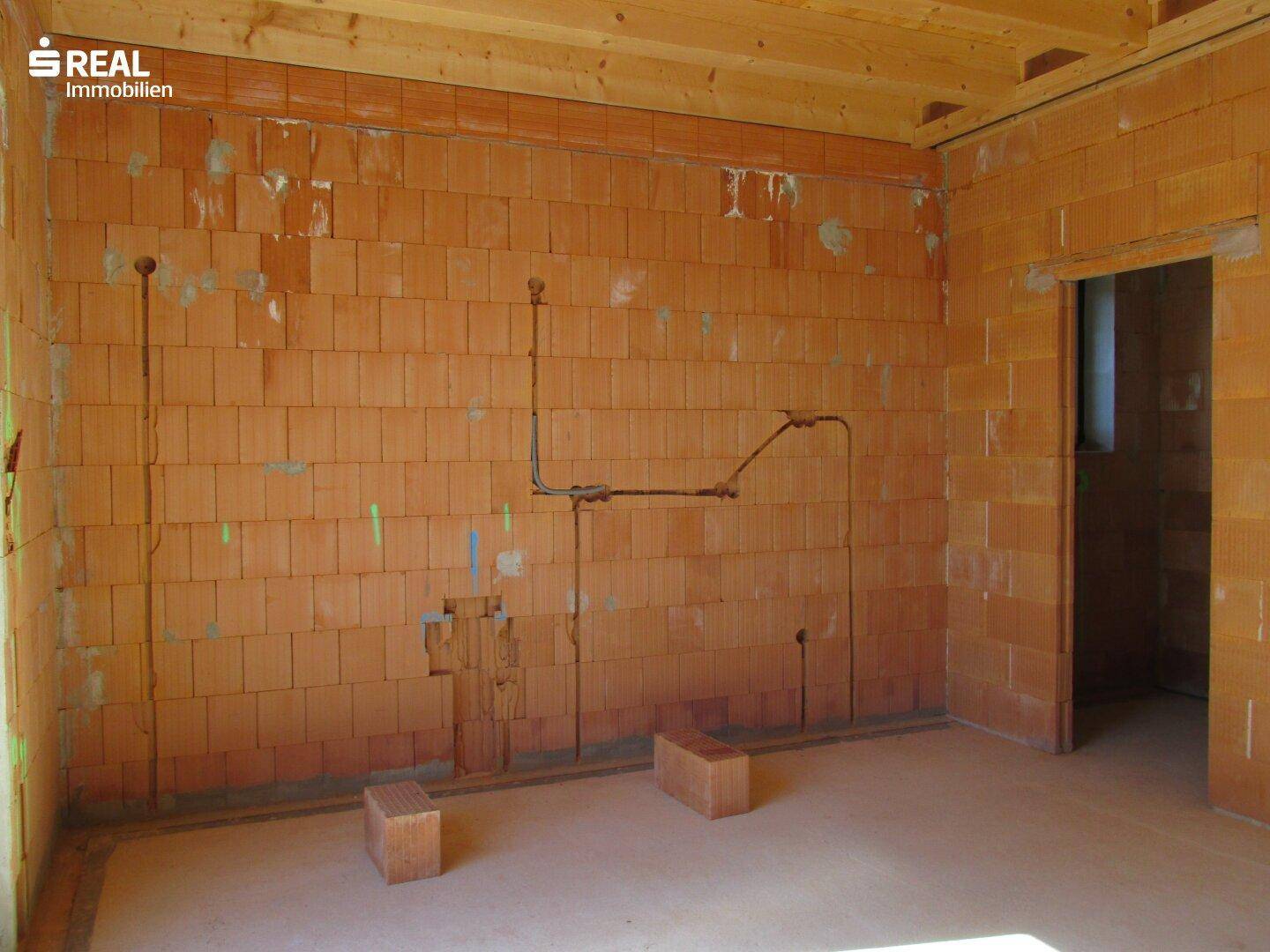 Rohbauzimmer mit Ziegelwänden und vorbereiteten Installationen für Elektrik und Sanitär.