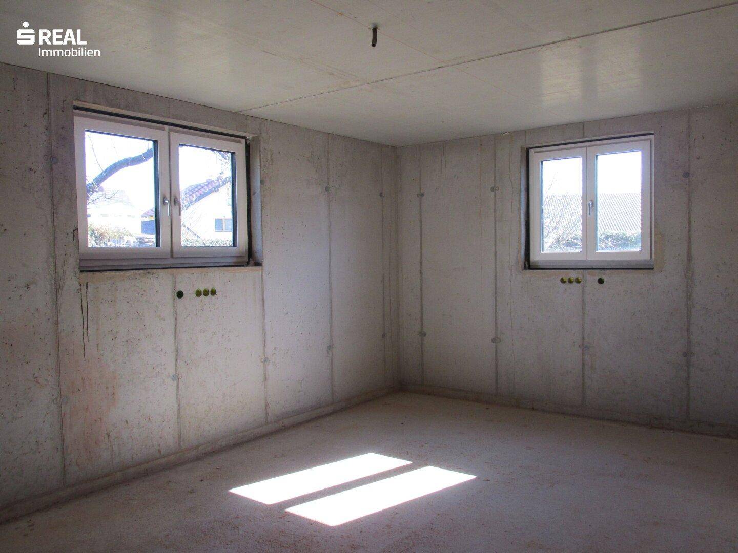 Heller Kellerraum mit zwei Fenstern und Betonwänden, die viel natürliches Licht hereinlassen.
