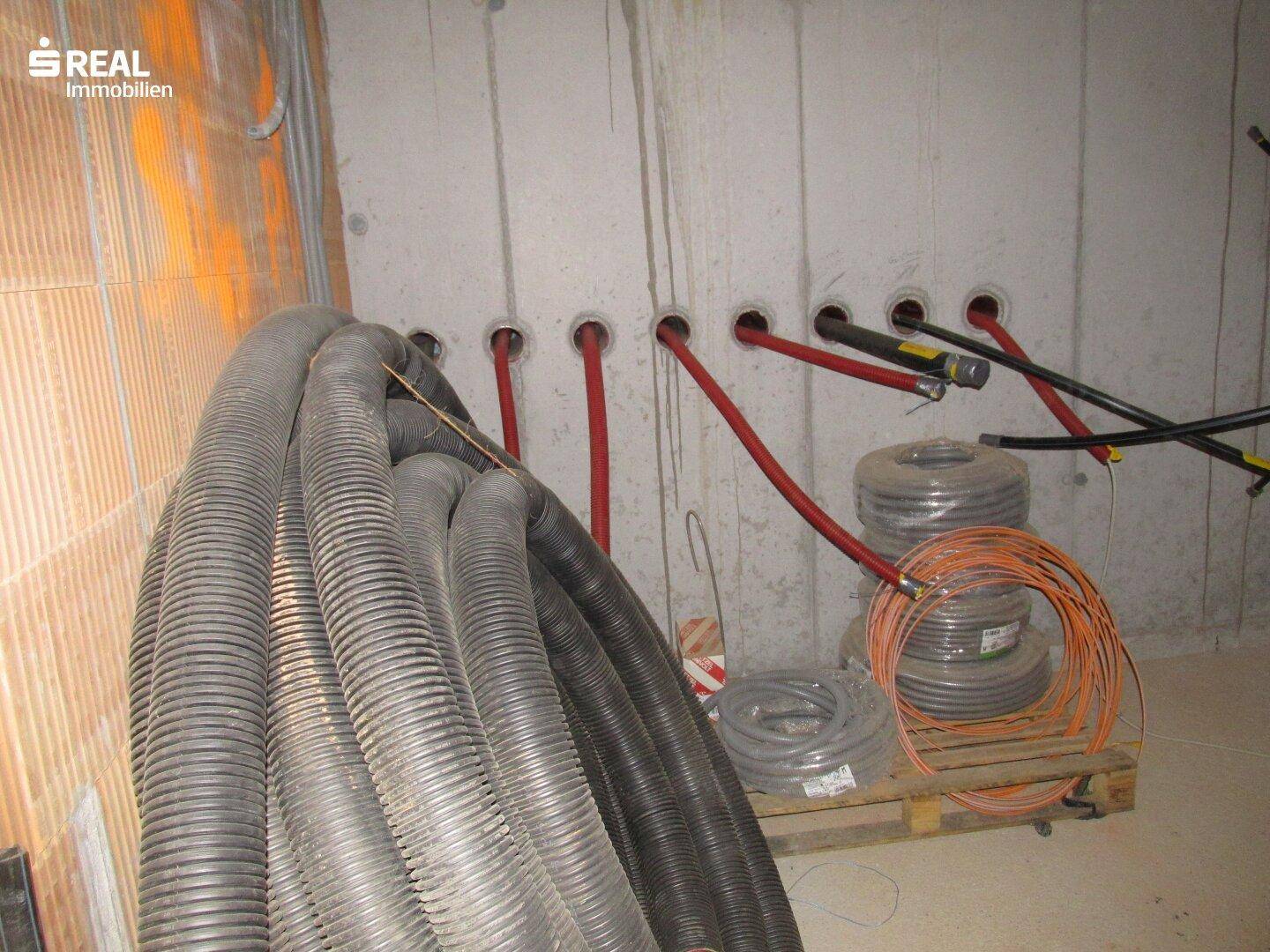 Kellerraum mit vorbereiteten Installationen für Rohre und Kabel, die aus der Wand kommen.