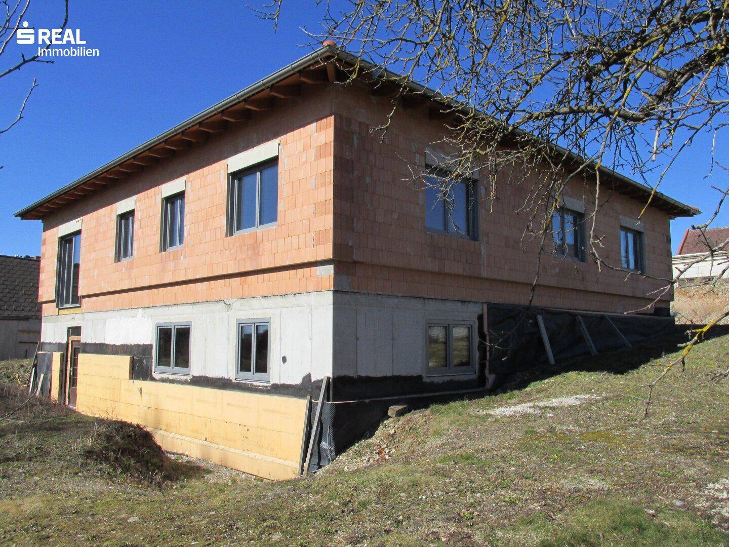 Rohbauansicht des Hauses mit sichtbarem Kellergeschoss und Ziegelmauerwerk im Obergeschoss.