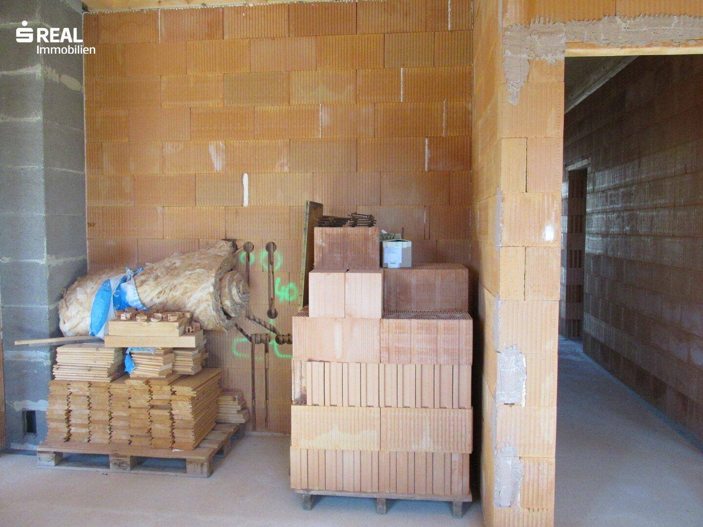 Innenraum im Rohbau mit Baumaterialien und Ziegelstapeln, die auf die Verarbeitung warten.