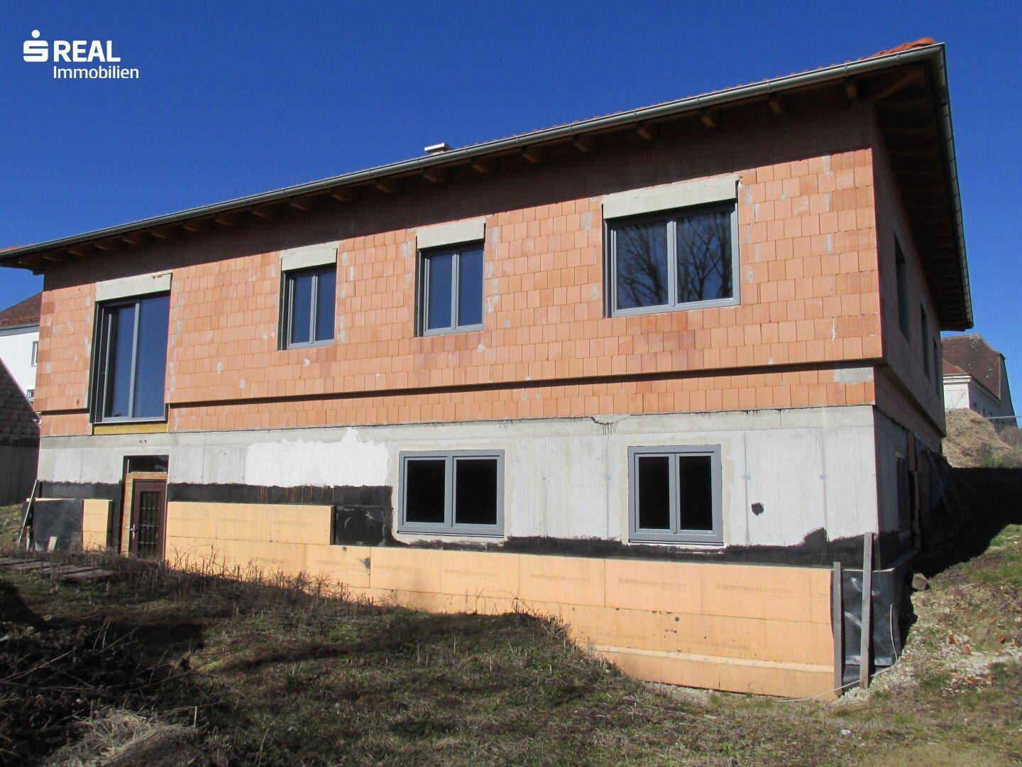 Seitenansicht des Neubaus mit Kellerfenstern und der vorbereiteten Fassade für die Dämmung.