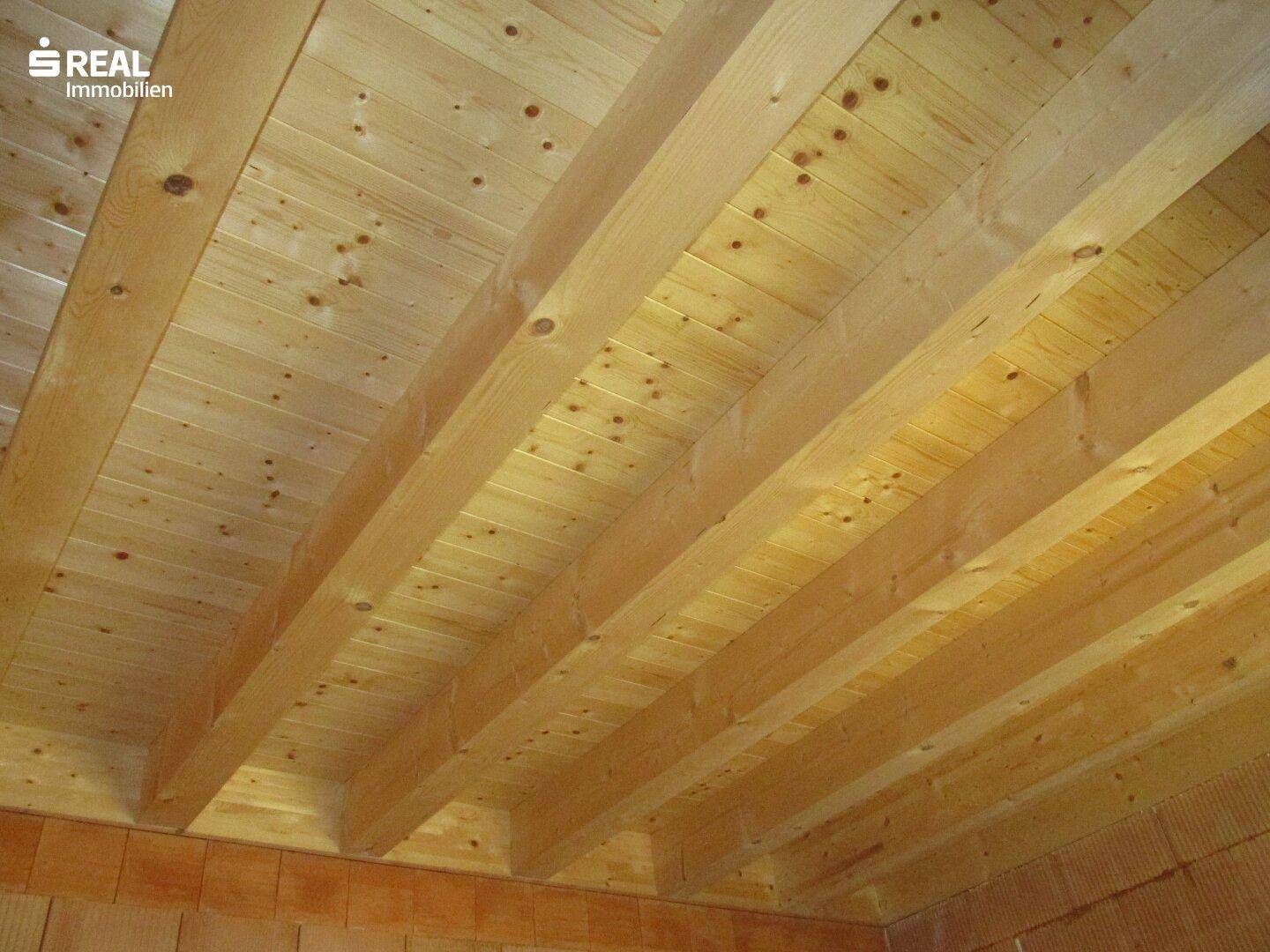 Sichtbare Holzdeckenbalken und Holzverkleidung im Innenraum, Teil der Dachkonstruktion.