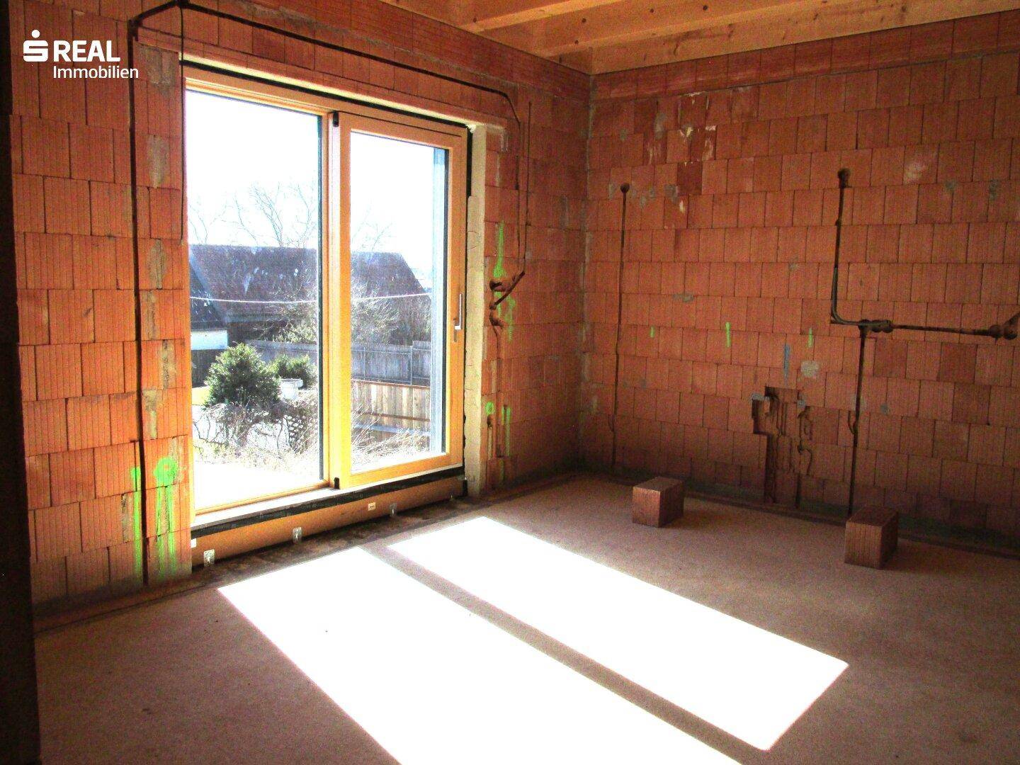 Heller Innenraum im Rohbau mit großen Fenstern und sichtbaren Ziegelwänden, viel Tageslicht.