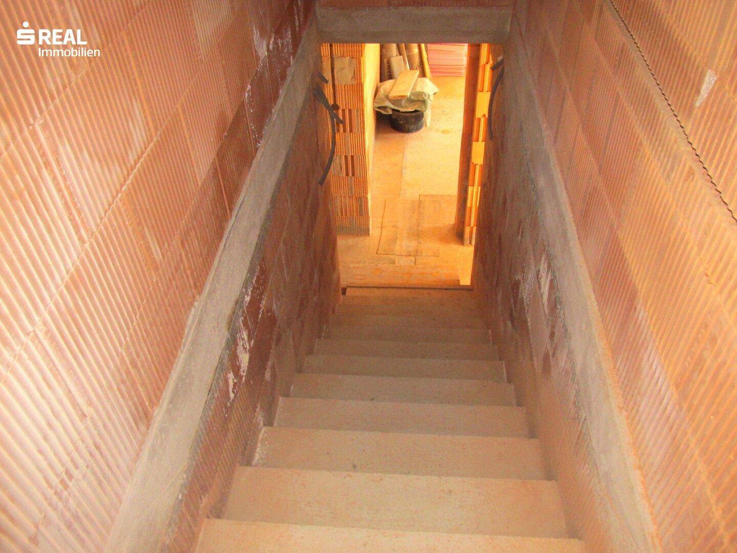 Treppe führt hinunter in den Kellerbereich des Rohbaus, mit sichtbaren Ziegelwänden.