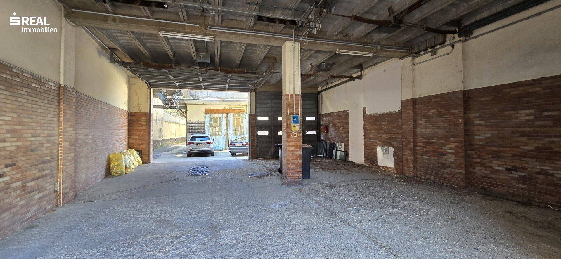 Große Lagerhalle mit Betonboden, Ziegelwänden und Rolltoren am Ende des Raumes.