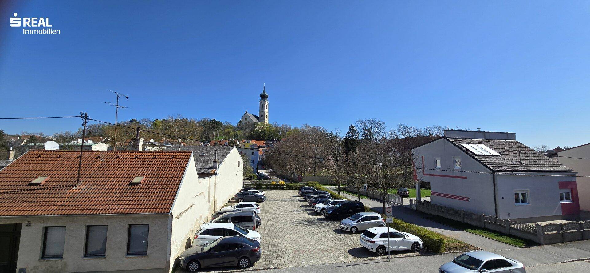 Weitläufiger Blick über die Dächer der Stadt mit einem Kirchturm auf einem Hügel im Hintergrund.