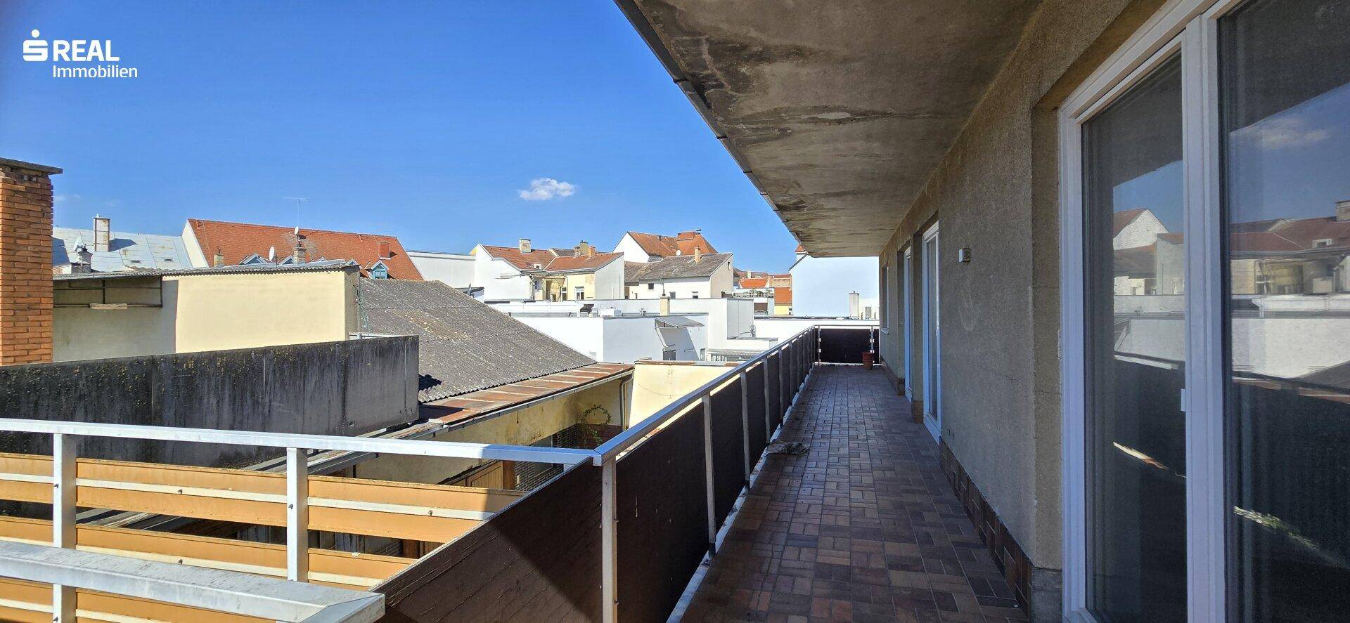 Langer Balkon mit Fliesenboden und Blick über die Dächer der umliegenden Gebäude.