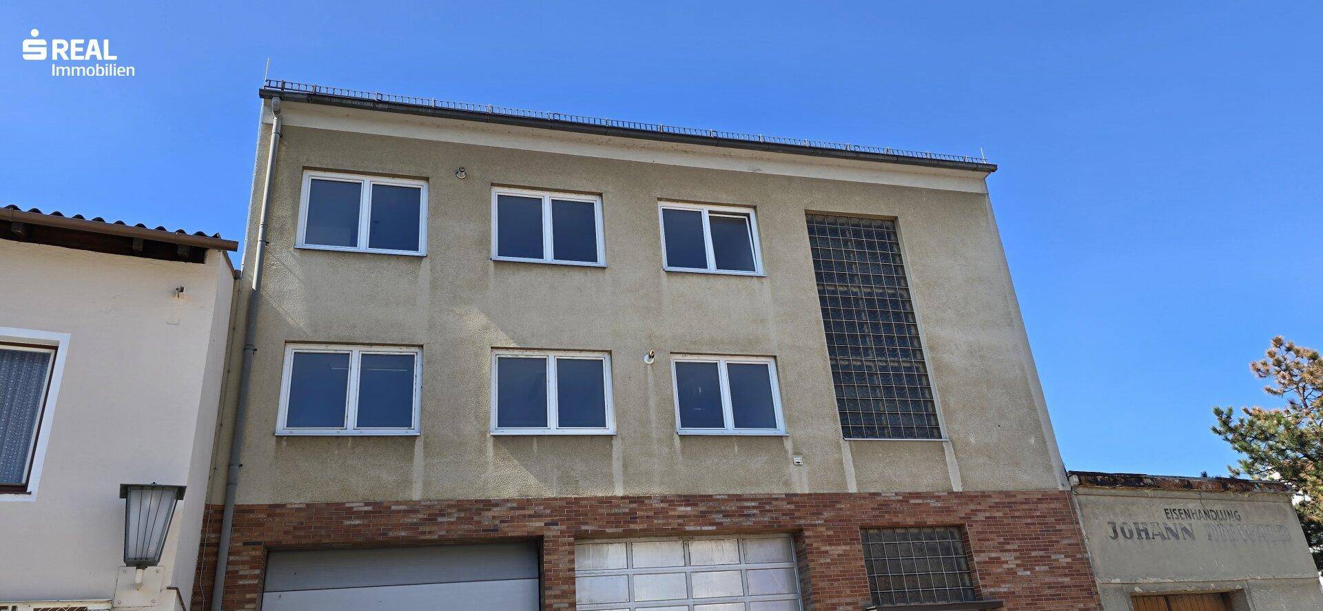 Fassade eines Mehrfamilienhauses mit mehreren Fenstern und einem großen Gitterfenster im Erdgeschoss.