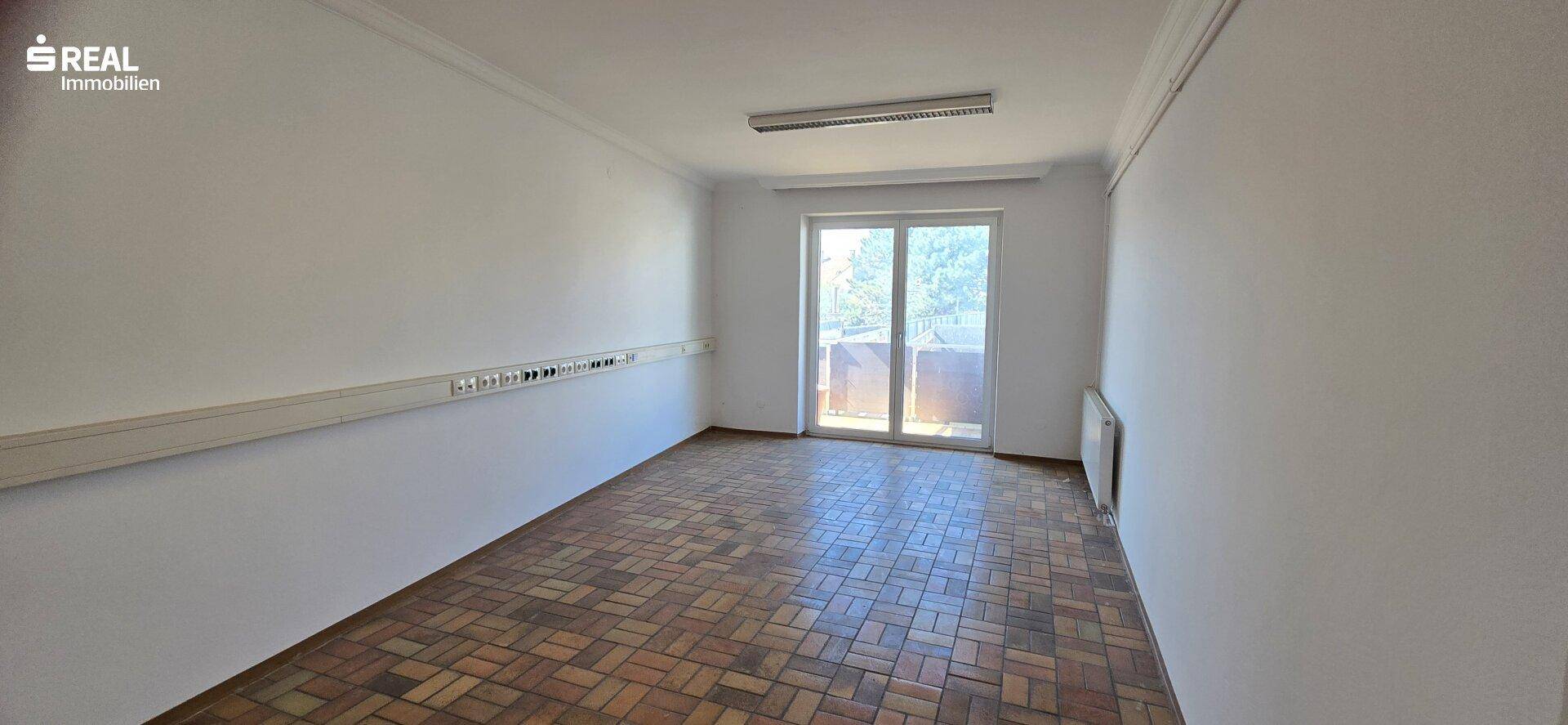 Helles Zimmer mit Parkettboden und einer großen Fenstertür, die viel Tageslicht hereinlässt.