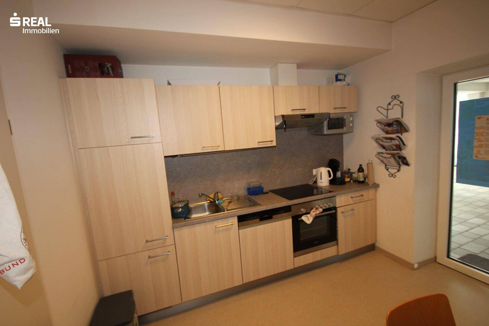 Funktionale Einbauküche mit hellen Holzfronten, Kochfeld, Backofen und Mikrowelle.