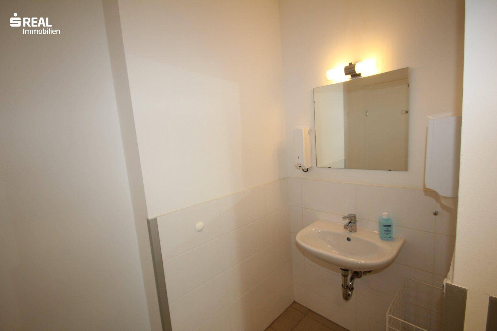 Kleines WC mit Waschbecken, Spiegel und Seifenspender, einfach und funktional.