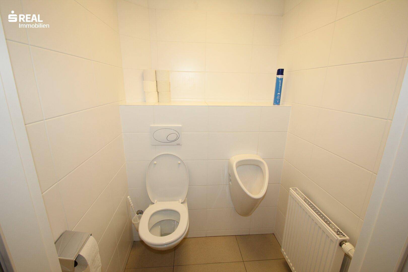 Herren-WC mit wandhängender Toilette und Urinal, gefliest und gut gepflegt.