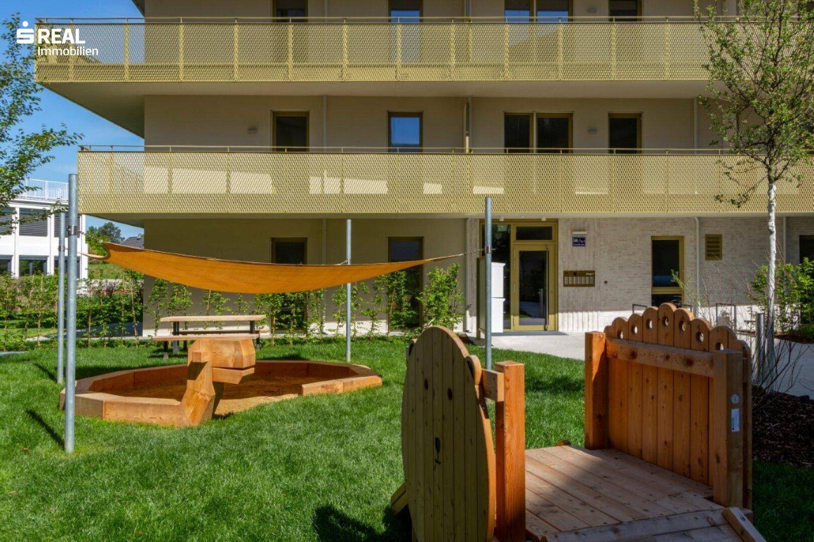Kinderspielplatz mit Sandkasten und Sonnensegel direkt vor dem modernen Wohngebäude.