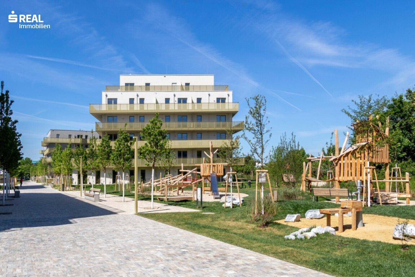 Weitläufige Außenanlage mit modernen Wohngebäuden und einem naturnahen Kinderspielplatz.