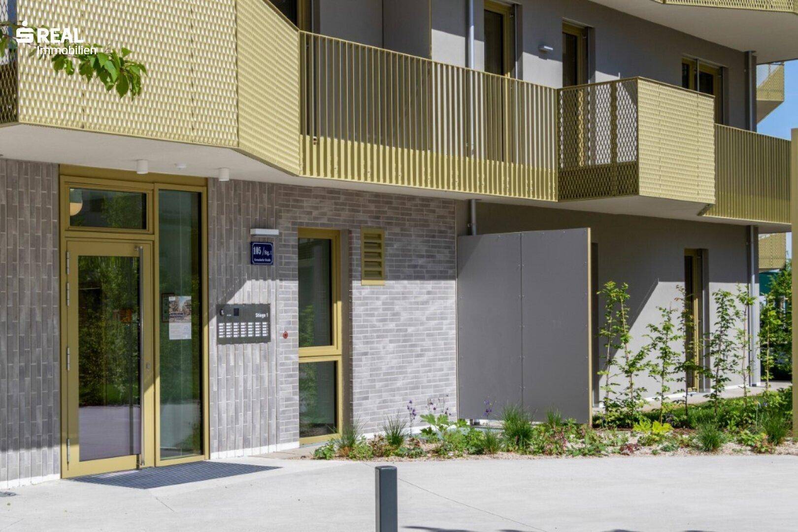 Eingangsbereich eines modernen Wohngebäudes mit Glastür, Gegensprechanlage und dekorativen Ziegelsteinelementen.