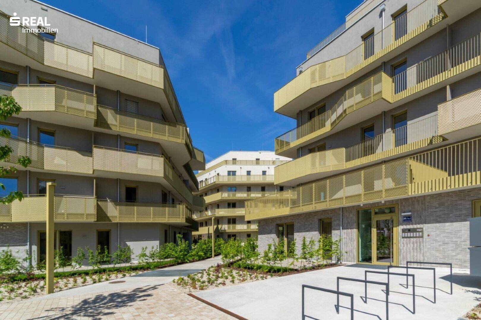 Blick zwischen zwei modernen Wohngebäuden mit zahlreichen Balkonen und gepflegten Außenanlagen.