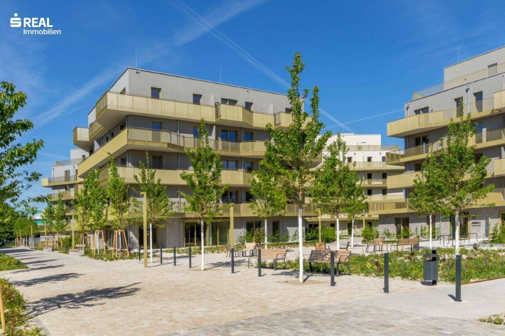 Ansicht eines modernen Wohnkomplexes mit mehreren Gebäuden und begrünten Außenbereichen.
