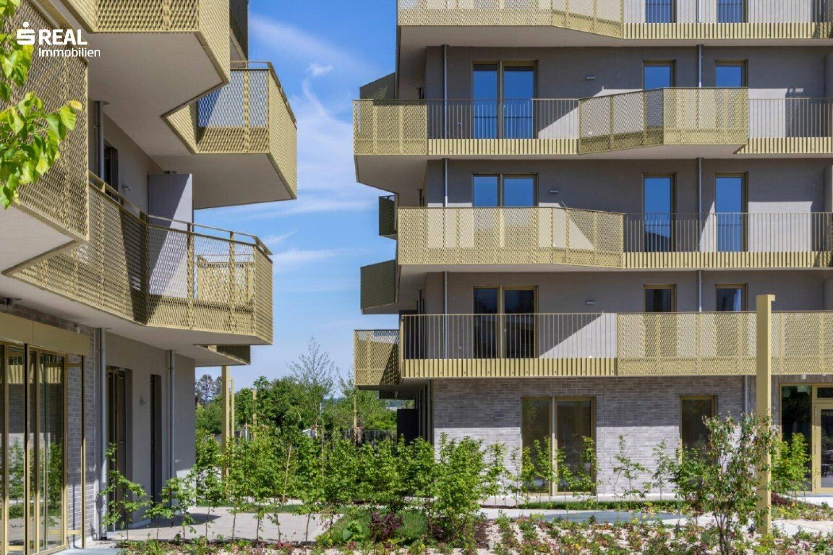 Detailansicht der modernen Fassade mit goldfarbenen Balkonen und großen Fenstern.