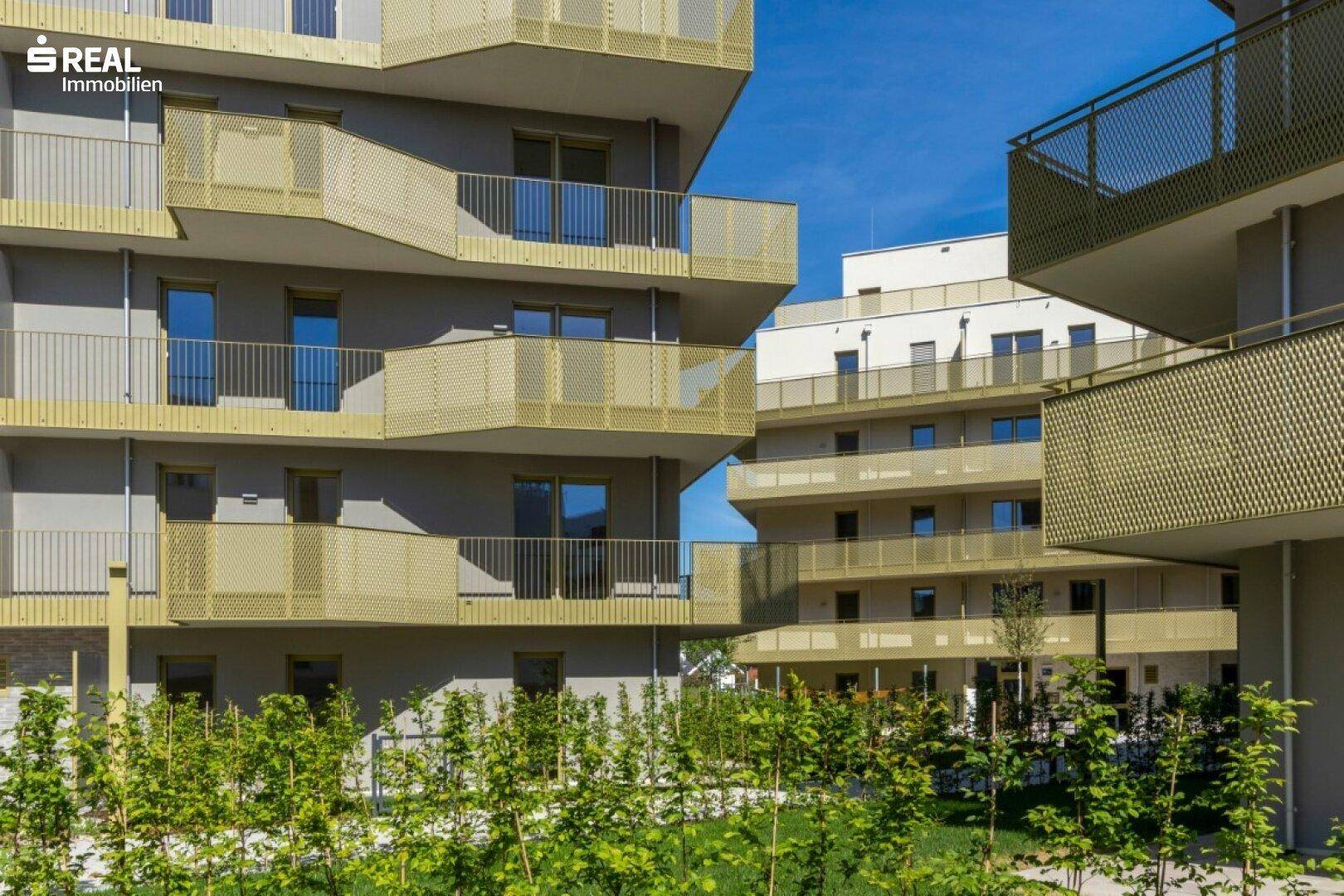Ansicht von modernen Wohngebäuden mit vielen Balkonen und üppiger Bepflanzung im Vordergrund.