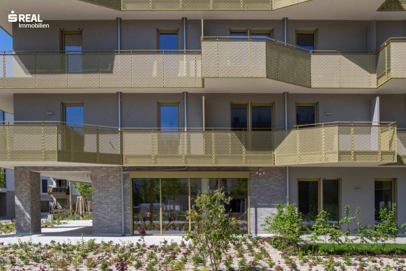 Erdgeschossfassade mit großen Fensterfronten und Zugang zu kleinen privaten Grünflächen.