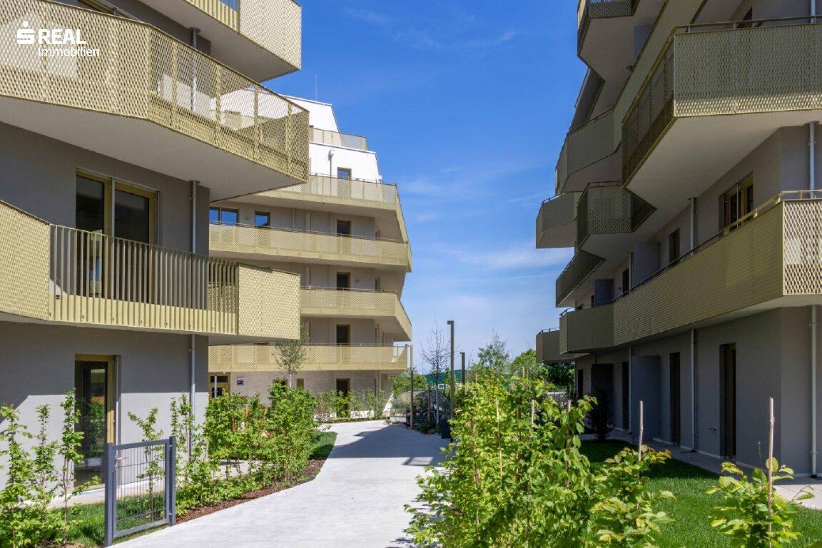 Blick zwischen zwei modernen Wohngebäuden mit markanten Balkonen und gepflegten Grünflächen dazwischen.