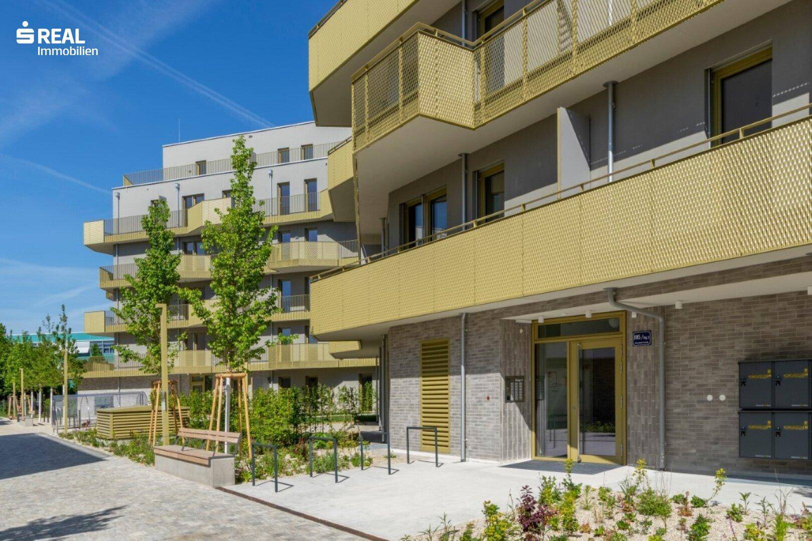 Eingangsbereich eines modernen Apartmentgebäudes mit Briefkästen und Fahrradständern im Freien.