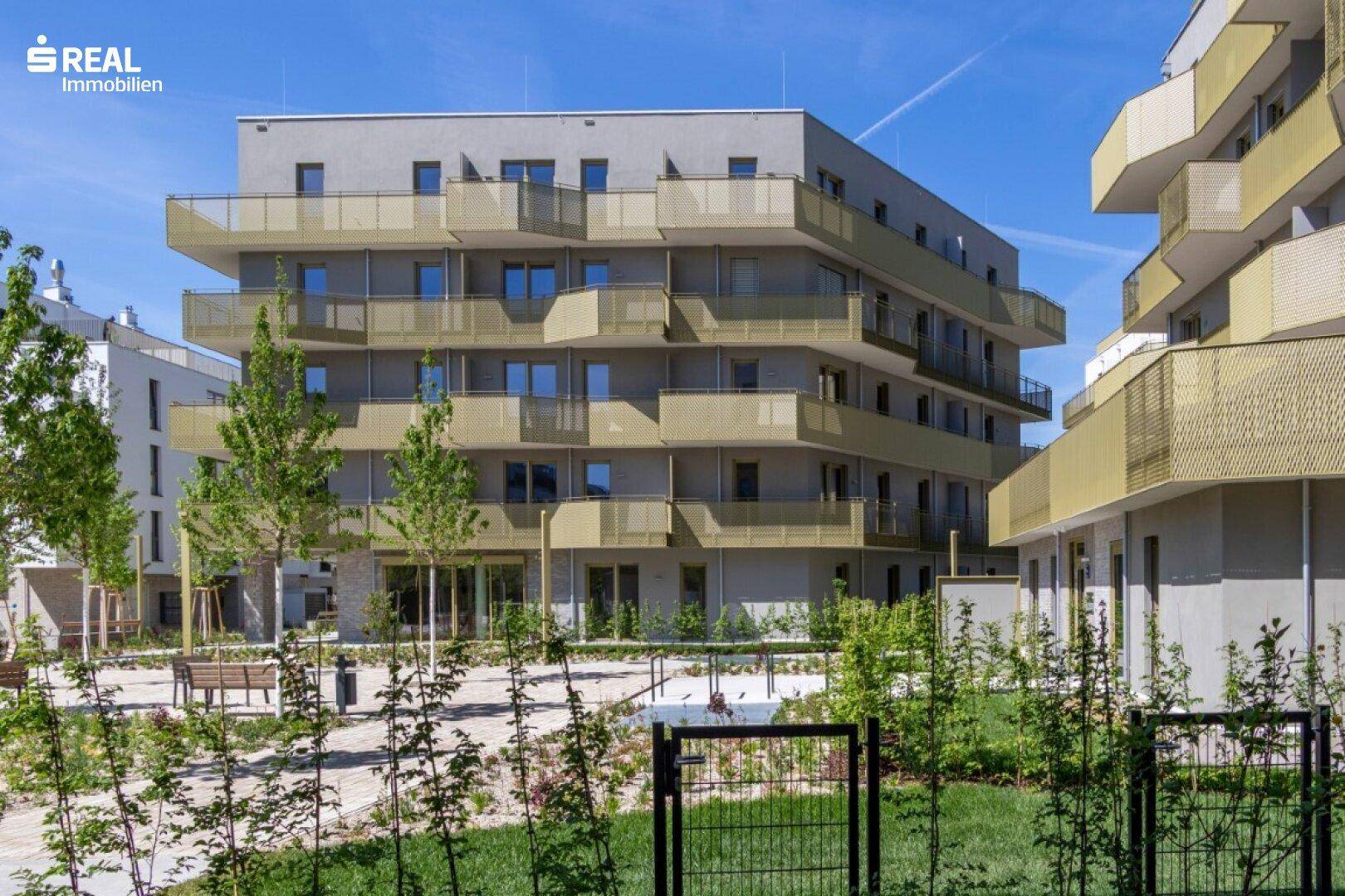 Modernes Apartmentgebäude mit mehreren Balkonen und grüner Bepflanzung im Vordergrund.