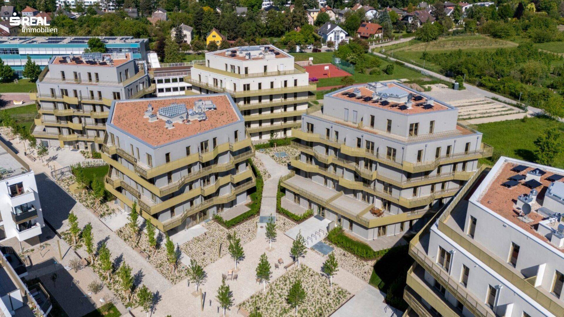 Luftaufnahme einer modernen Wohnanlage mit mehreren Apartmentgebäuden und Grünflächen.
