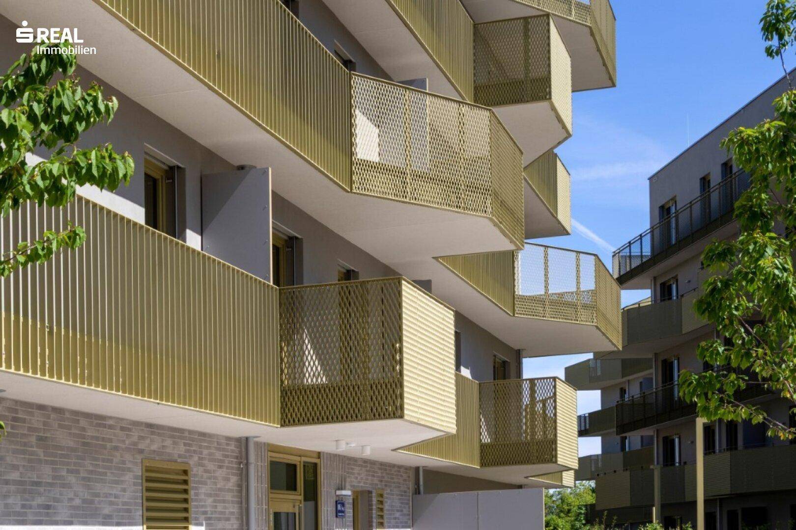 Detailansicht der modernen, gelb-goldenen Balkone mit perforierten Geländern an der Gebäudefassade.