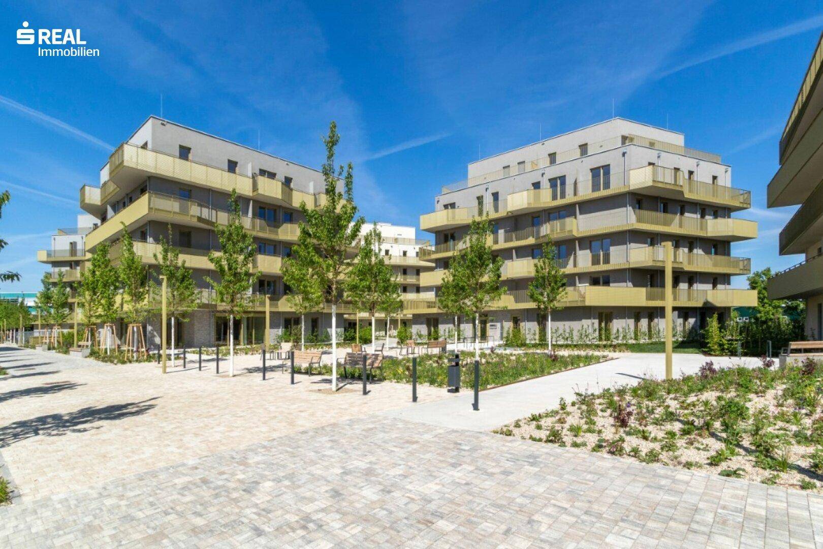 Weitläufige Außenanlage eines modernen Wohnkomplexes mit mehreren Gebäuden und Grünflächen.