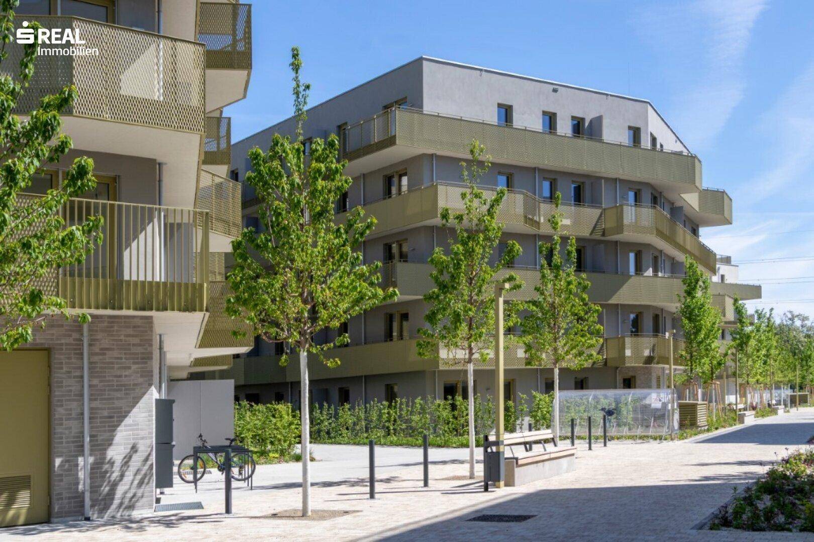 Moderne Wohnanlage mit mehreren Gebäuden, Balkonen und begrünten Außenbereichen unter blauem Himmel.