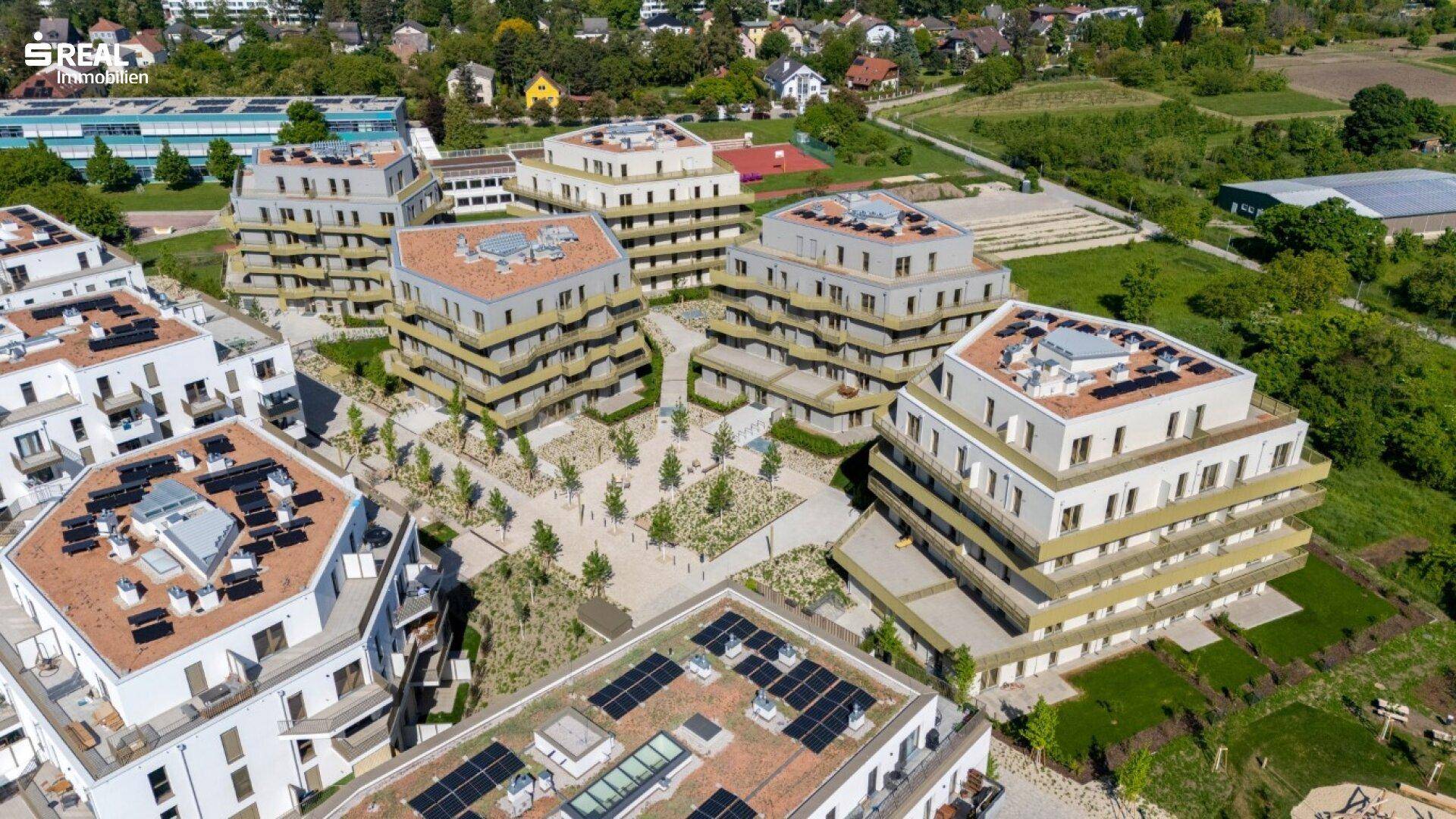 Luftaufnahme einer modernen Wohnsiedlung mit mehreren Gebäuden, Balkonen und begrünten Dächern.