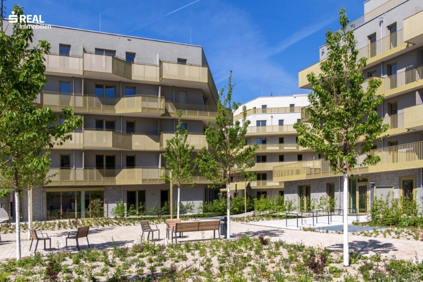 Mehrere moderne Wohngebäude umgeben einen begrünten Innenhof mit Bäumen und Sitzgelegenheiten.