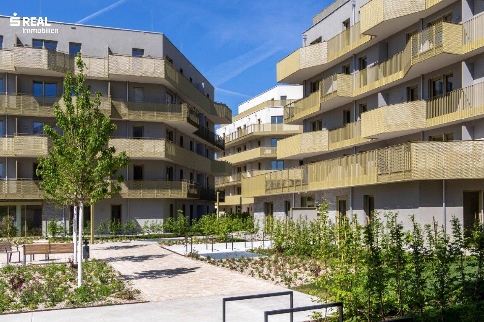 Moderne Wohngebäude mit goldfarbenen Balkonen und einem gepflegten, begrünten Innenhof.