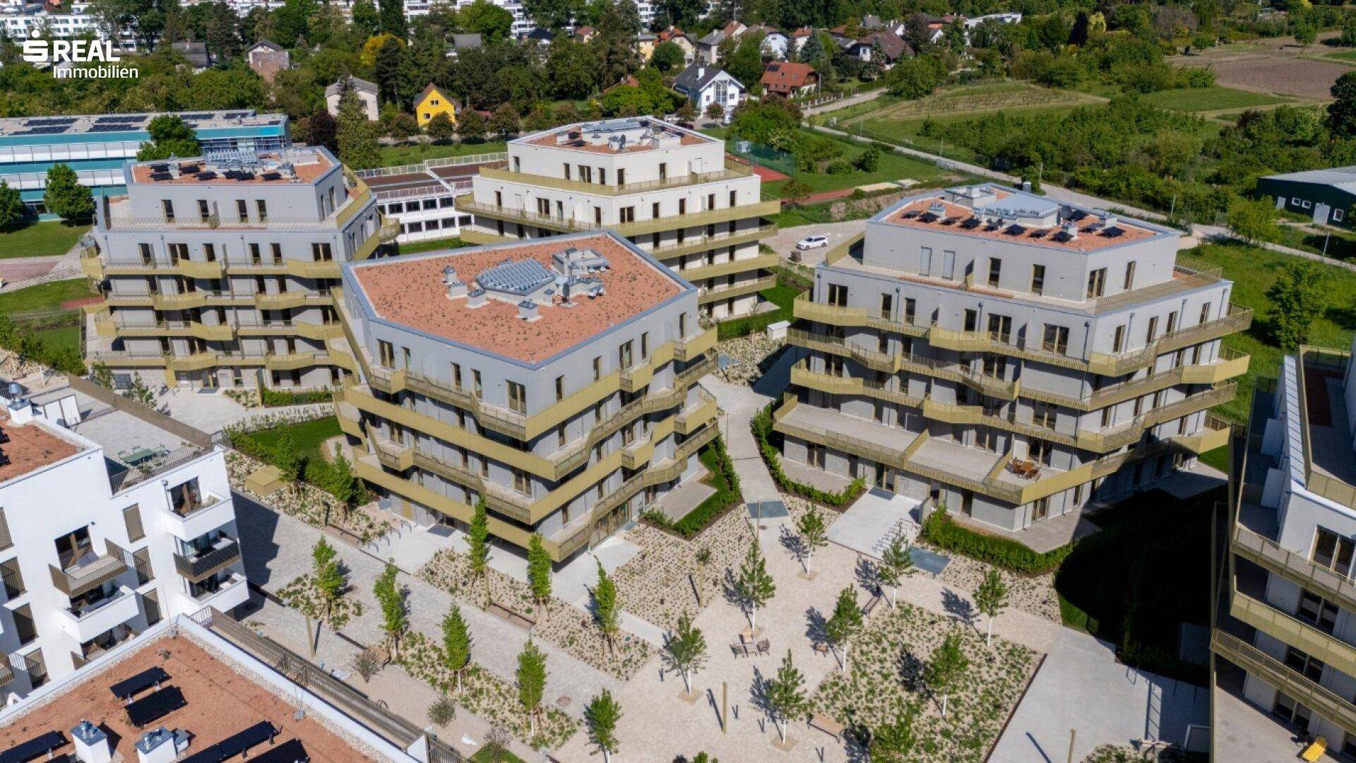 Luftaufnahme eines modernen Wohnkomplexes mit mehreren Gebäuden und begrünten Außenbereichen.