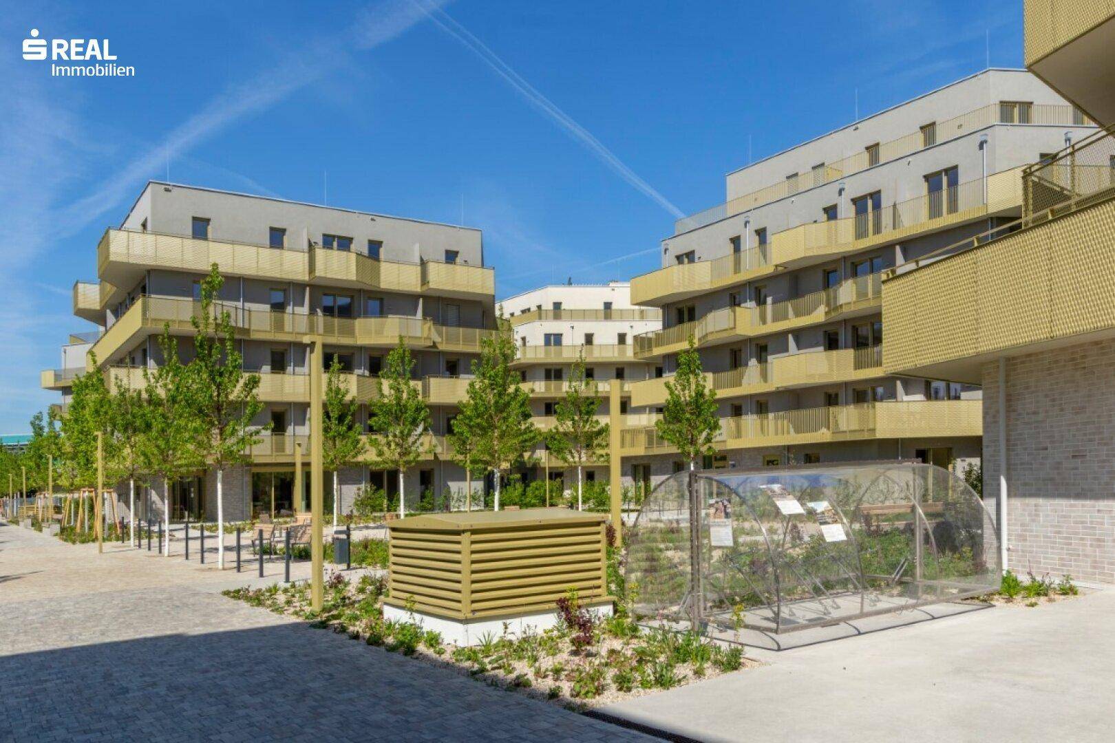 Ansicht der modernen Wohngebäude mit Balkonen und einem Gemeinschaftsgartenbereich mit Hochbeeten.