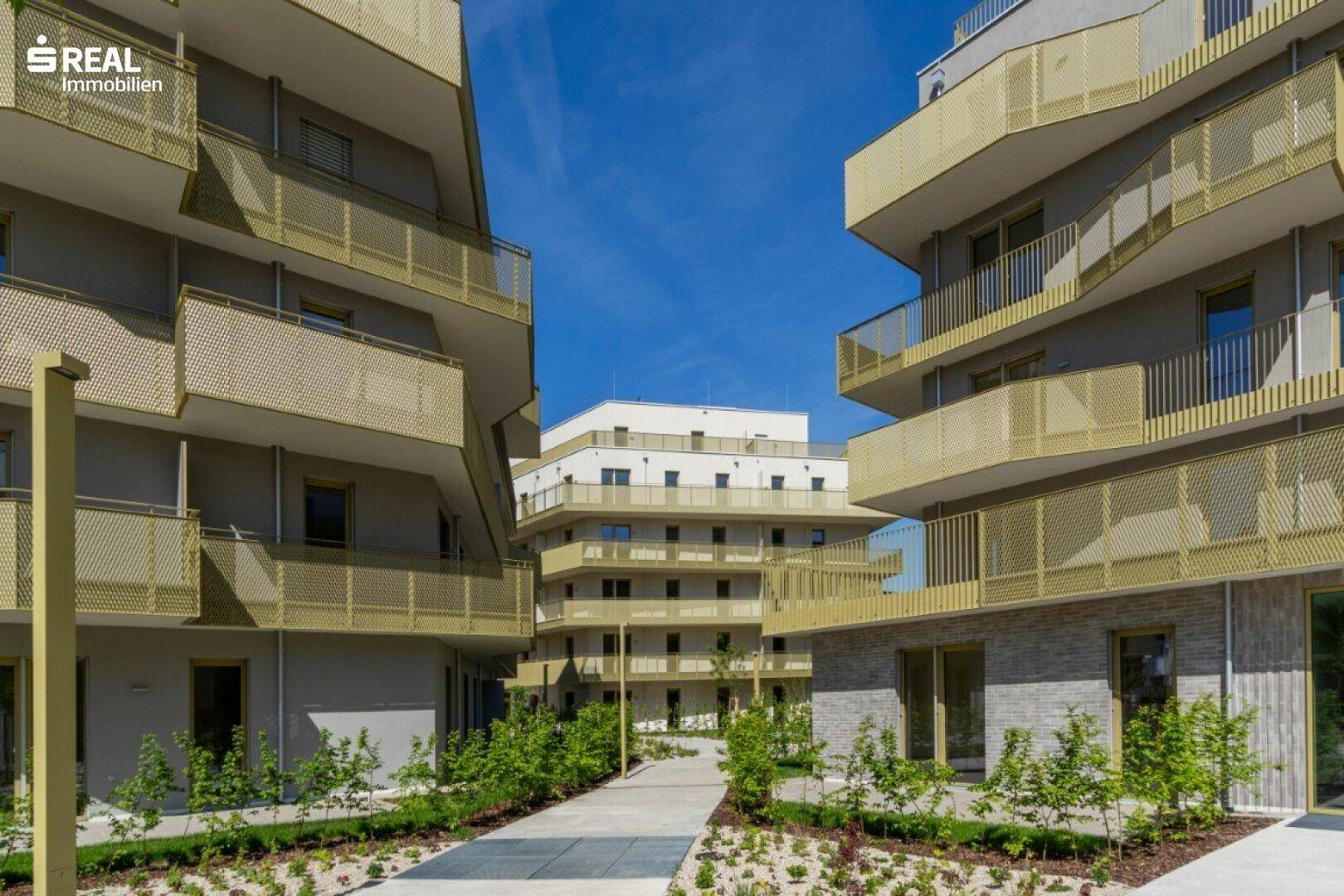 Moderne Wohngebäude mit markanten Balkonen und einem hellen Innenhof unter klarem Himmel.