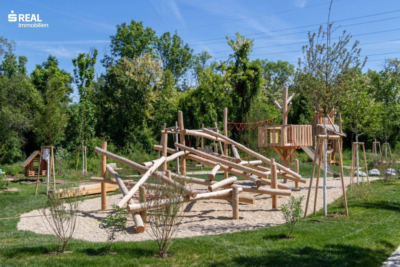 Großer, naturnaher Spielplatz mit Holzspielgeräten und viel Grünfläche für Kinder.