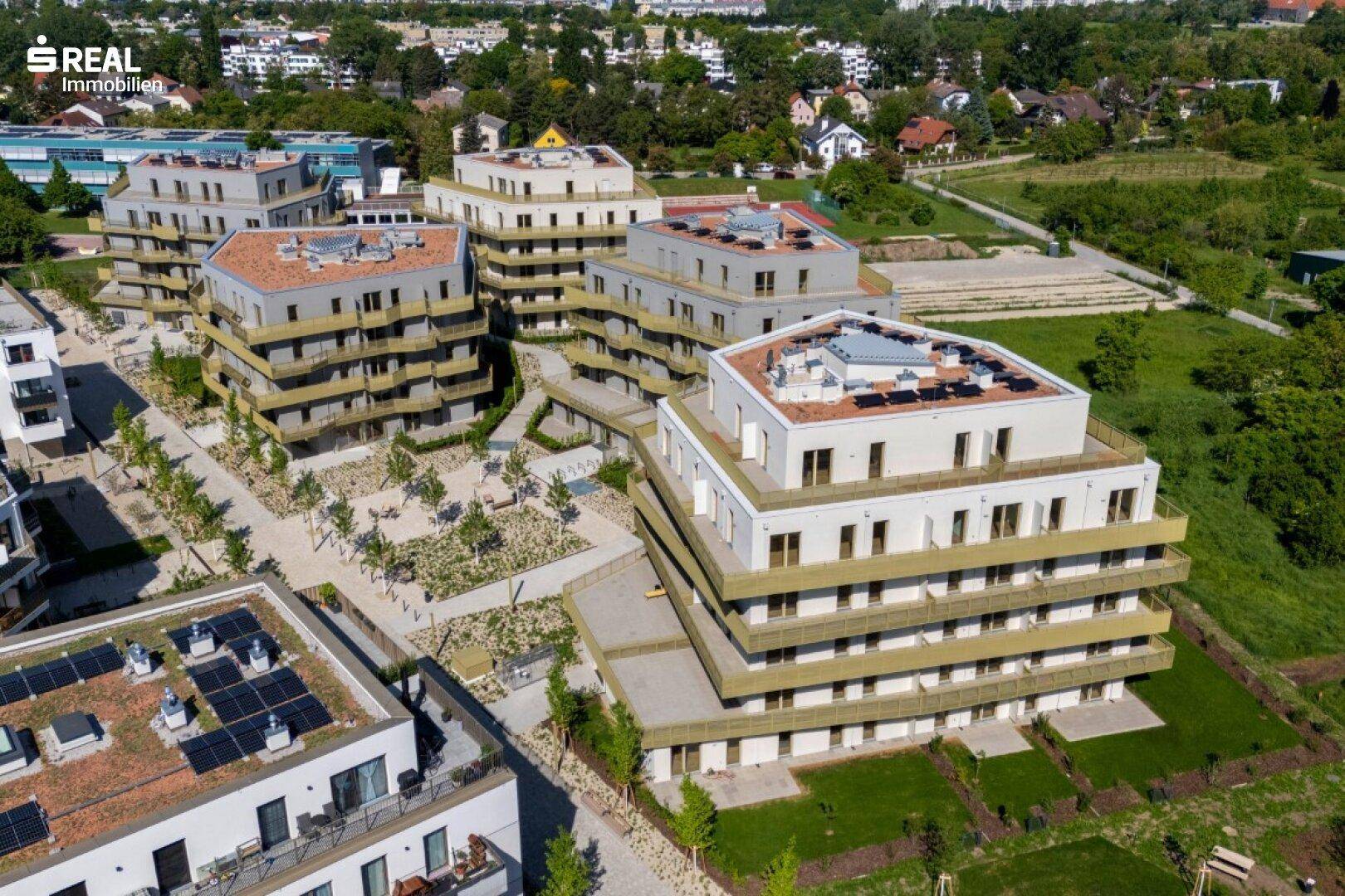 Luftaufnahme des modernen Wohnkomplexes mit mehreren Gebäuden, Grünflächen und Photovoltaikanlagen.