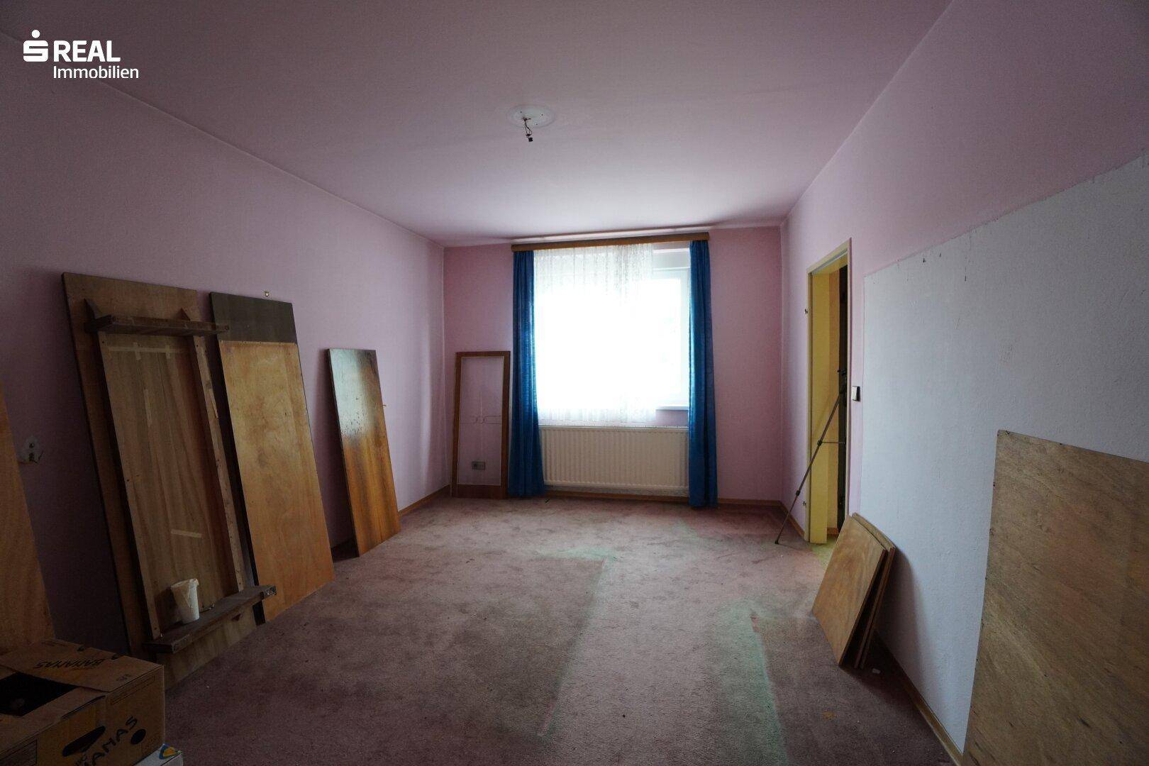Leeres Zimmer mit rosa Wänden, Teppichboden und einem Fenster mit blauen Vorhängen.