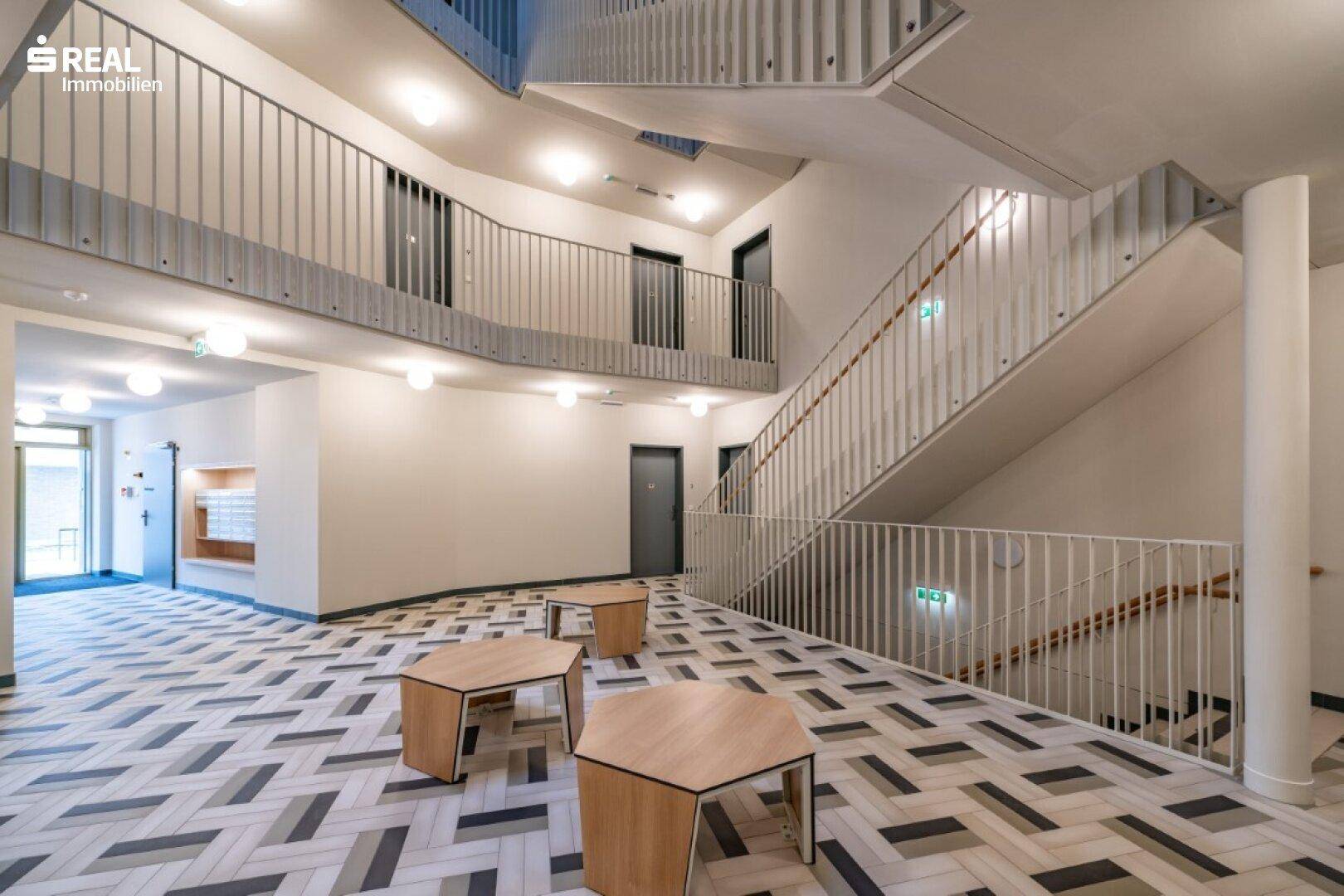 Großzügiger Eingangsbereich mit Treppenhaus, modernen Sitzgelegenheiten und stilvollem Fliesenboden.